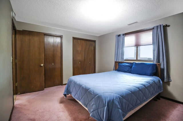 bedroom featuring carpet floors, multiple closets, and a textured ceiling