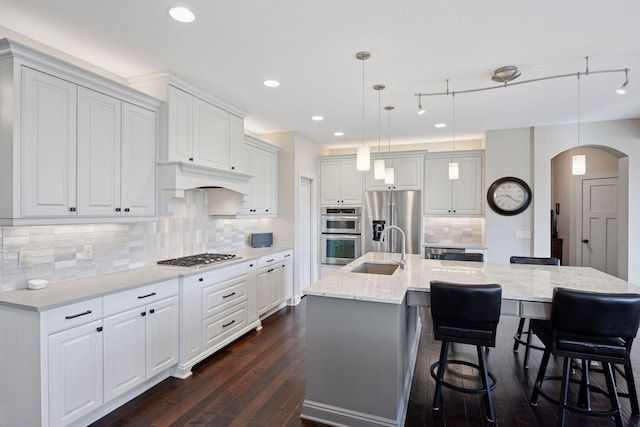 2971 Fairway Dr, Chaska, MN 55318 - kitchen with a sink, appliances with stainless steel finishes, arched walkways, dark wood finished floors, and a center island with sink