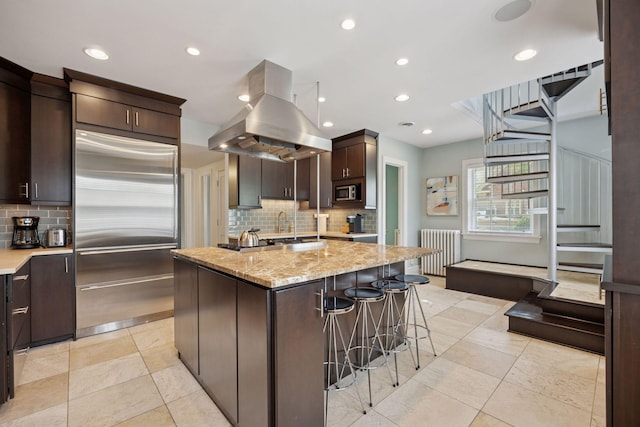 1785 Dupont Ave S, Minneapolis, MN 55403 - kitchen featuring built in appliances, radiator heating unit, island range hood, tasteful backsplash, and dark brown cabinetry