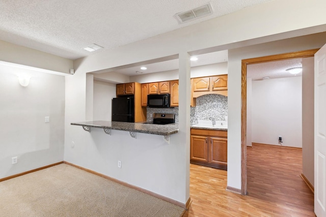 3613 Clare Downs Path, Rosemount, MN 55068 - kitchen with black appliances, a kitchen bar, a textured ceiling, backsplash, and brown cabinets