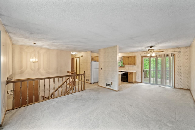 unfurnished living room with a textured ceiling, light colored carpet, a chandelier, ceiling fan, and wallpapered walls