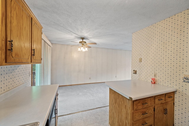 kitchen with ceiling fan, light countertops, brown cabinets, a textured ceiling, and light colored carpet