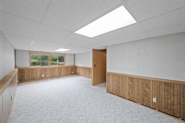 carpeted empty room featuring a drop ceiling, wooden walls, and a wainscoted wall