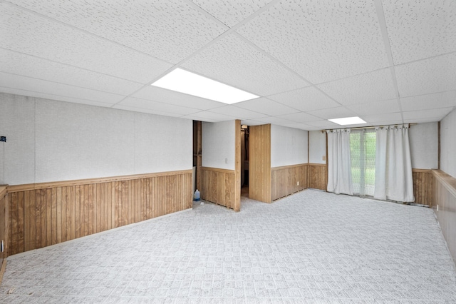 below grade area with a wainscoted wall, a drop ceiling, wood walls, and carpet floors