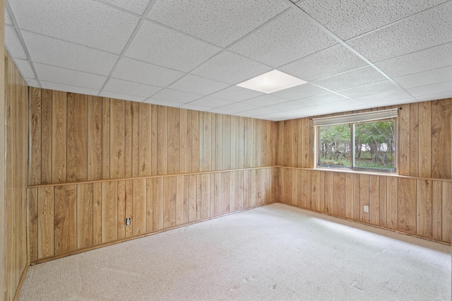 unfurnished room with a paneled ceiling, wooden walls, and carpet floors