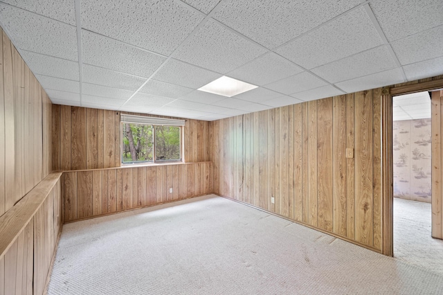 unfurnished room with a paneled ceiling, wood walls, and carpet flooring