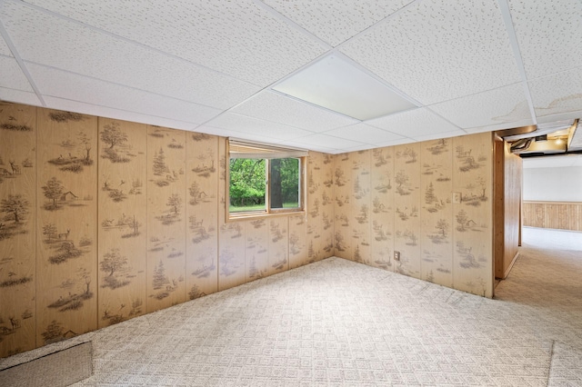 empty room with carpet, a paneled ceiling, and wooden walls