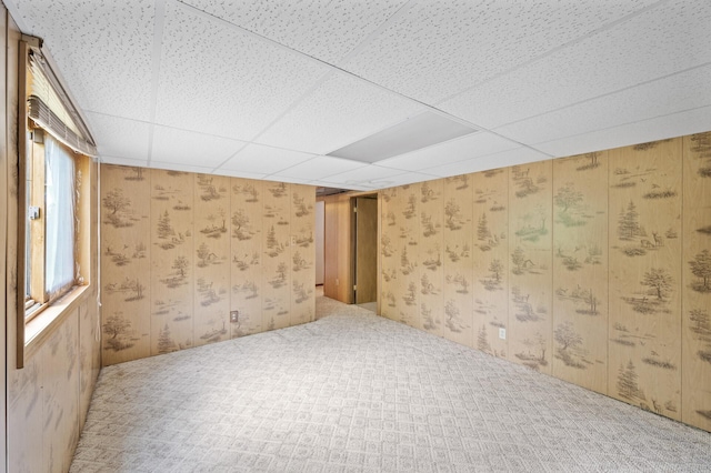 empty room with carpet flooring, a drop ceiling, and wooden walls