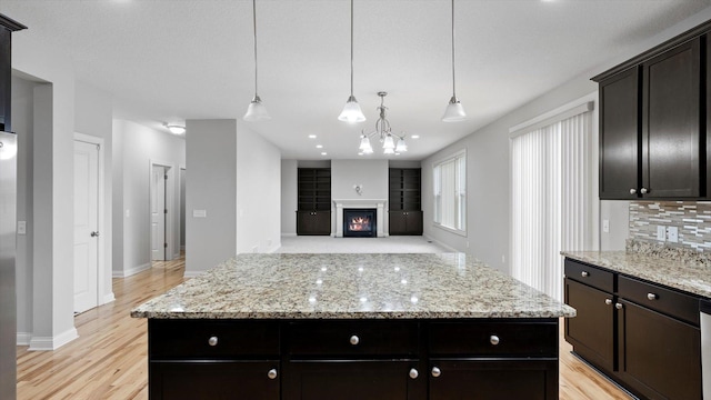 15365 Eagle Creek Way, Apple Valley, MN 55124 - kitchen featuring a kitchen island, a warm lit fireplace, light wood-style flooring, baseboards, and light stone countertops