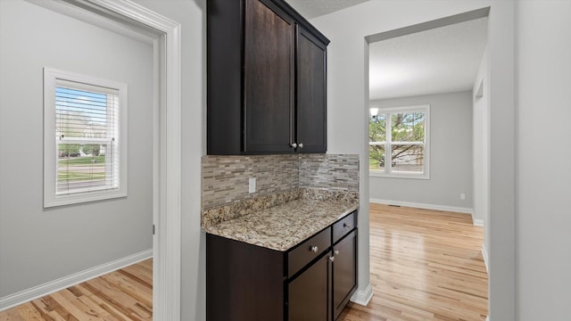 15365 Eagle Creek Way, Apple Valley, MN 55124 - kitchen with decorative backsplash, light wood-style floors, dark brown cabinetry, baseboards, and light stone countertops