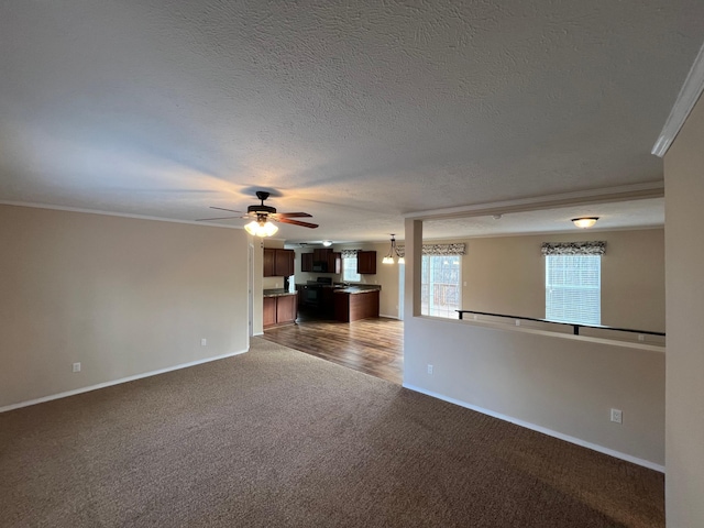 unfurnished living room with carpet flooring, a ceiling fan, baseboards, a textured ceiling, and crown molding