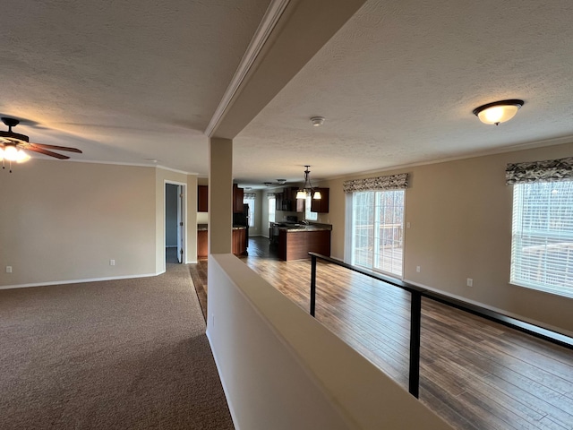 unfurnished living room featuring a textured ceiling, ornamental molding, ceiling fan, and baseboards
