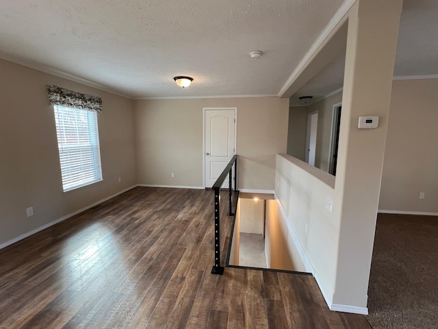 empty room with wood finished floors, baseboards, ornamental molding, a smoke detector, and a textured ceiling