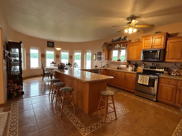 14620 Thomas Rd, Lake Park, MN 56554 - kitchen with stainless steel range with electric stovetop, a kitchen breakfast bar, tile patterned floors, ceiling fan, and brown cabinetry