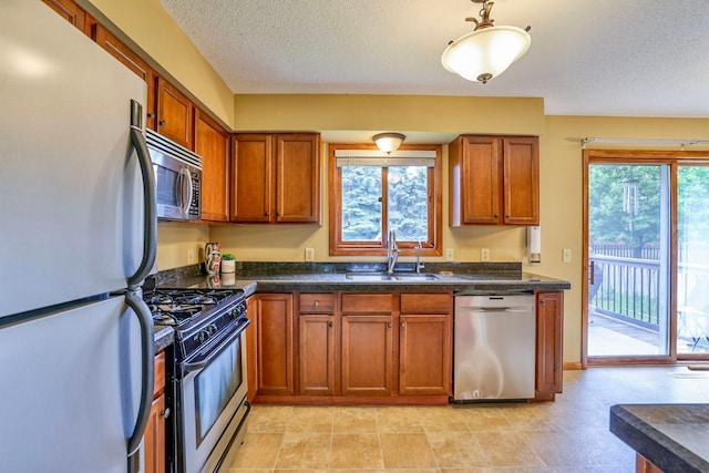 11215 Sumter Ave N, Champlin, MN 55316 - kitchen featuring stainless steel appliances, a sink, brown cabinets, dark countertops, and a textured ceiling