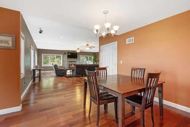 dining space with a large fireplace, a chandelier, ceiling fan, and wood finished floors