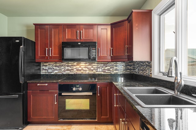 kitchen featuring black appliances, a sink, reddish brown cabinets, and dark stone counters