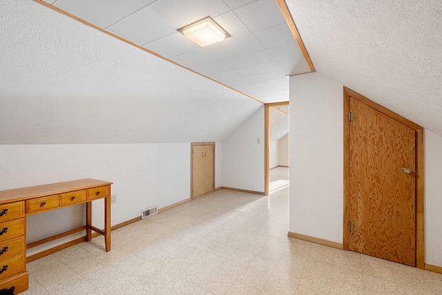 additional living space featuring light flooring, lofted ceiling, baseboards, and a textured ceiling