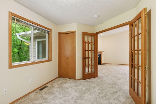 934 105th Ave NW, Coon Rapids, MN 55433 - carpeted spare room featuring french doors, a textured ceiling, baseboards, and a fireplace with flush hearth