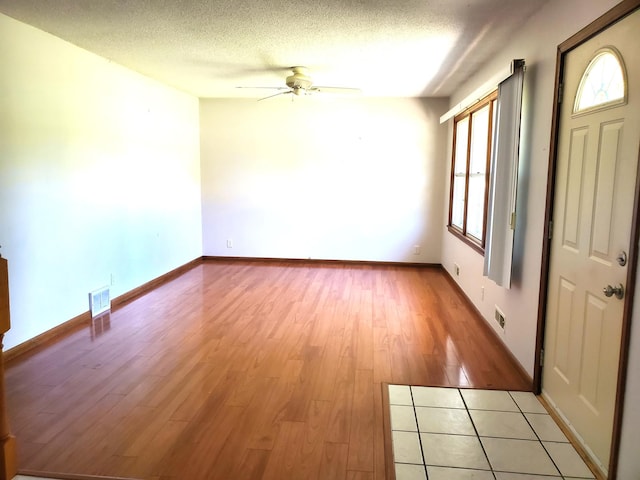 spare room featuring ceiling fan, light wood finished floors, a textured ceiling, and baseboards