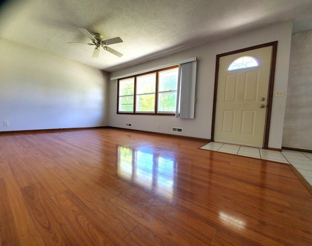 foyer with light wood-style floors, baseboards, a textured ceiling, and a ceiling fan