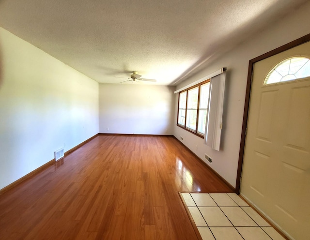 foyer with a textured ceiling, ceiling fan, light wood-type flooring, and baseboards
