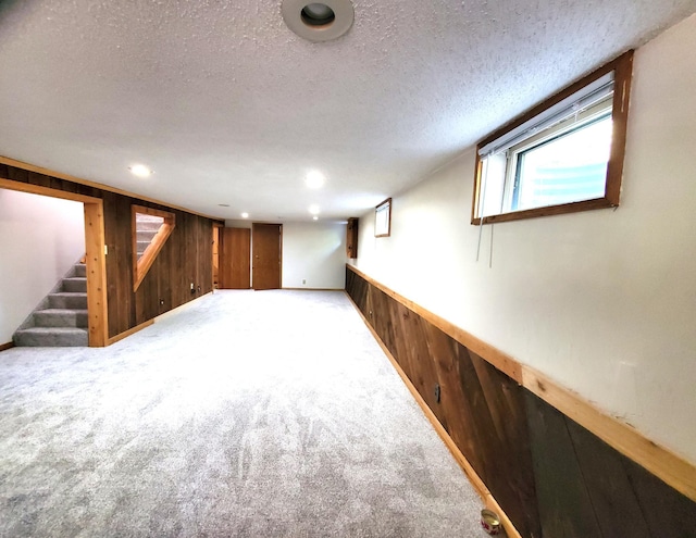 below grade area with wood walls, a textured ceiling, stairway, carpet, and a wainscoted wall