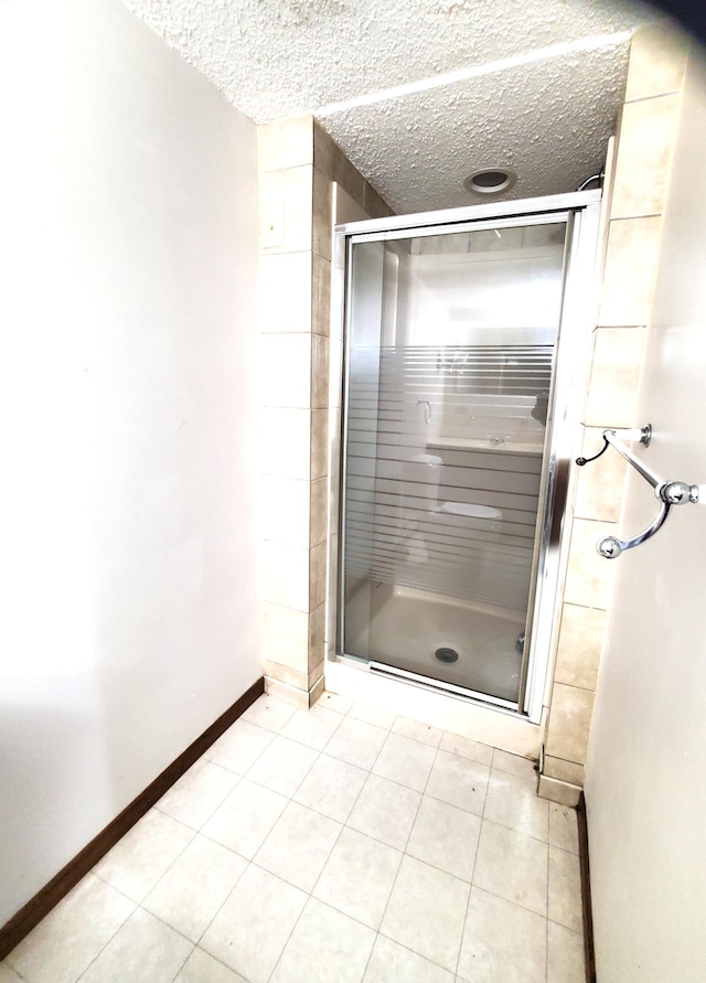 full bathroom with a stall shower, baseboards, tile patterned flooring, and a textured ceiling