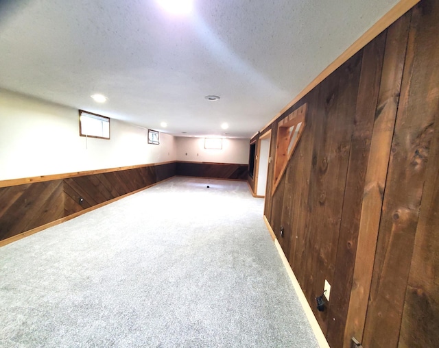below grade area with wooden walls, carpet, a textured ceiling, and baseboards