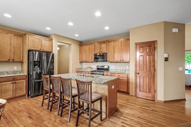 10025 Toledo Dr N, Brooklyn Park, MN 55443 - kitchen featuring appliances with stainless steel finishes, light wood-style flooring, a breakfast bar, a kitchen island with sink, and a textured ceiling