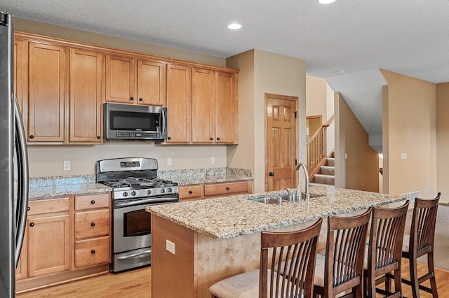 10025 Toledo Dr N, Brooklyn Park, MN 55443 - kitchen with appliances with stainless steel finishes, light wood-style floors, a sink, light stone counters, and a textured ceiling