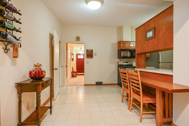 3760 Trenton Ln N, Plymouth, MN 55441 - kitchen with black microwave, freestanding refrigerator, brown cabinets, a textured ceiling, and stainless steel electric range oven