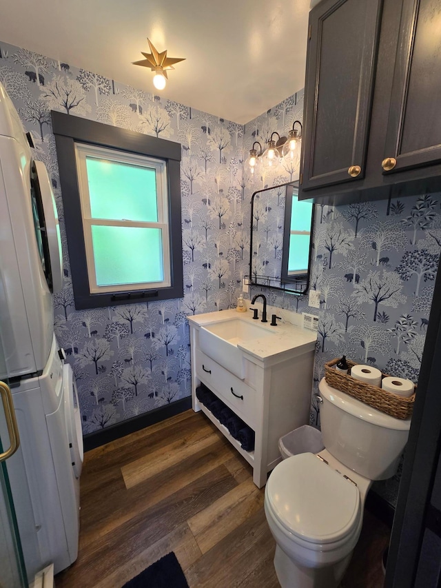8137 Hoyt Ave SW, Victor Twp, MN 55349 - bathroom featuring stacked washer / dryer, wood finished floors, toilet, vanity, and wallpapered walls