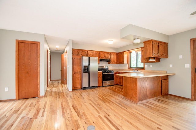 19715 Tyler St NW, Elk River, MN 55330 - kitchen with stainless steel appliances, a peninsula, light wood-style flooring, under cabinet range hood, and brown cabinetry