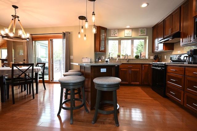 306 Windcrest Ln SE, New Prague, MN 56071 - kitchen with black gas range oven, under cabinet range hood, a kitchen breakfast bar, a chandelier, and dark wood-style floors
