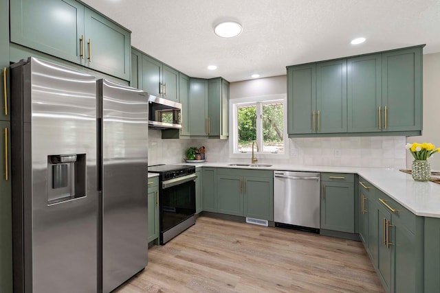 77 Emerson Ave W, West Saint Paul, MN 55118 - kitchen featuring stainless steel appliances, green cabinets, a sink, light wood finished floors, and backsplash