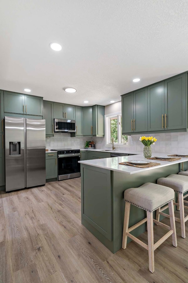77 Emerson Ave W, West Saint Paul, MN 55118 - kitchen with stainless steel appliances, green cabinets, light countertops, backsplash, and light wood finished floors
