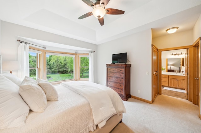 bedroom with light colored carpet, a tray ceiling, ensuite bath, ceiling fan, and baseboards