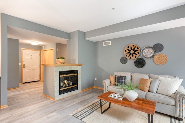 living room featuring a tiled fireplace, light wood-type flooring, and baseboards