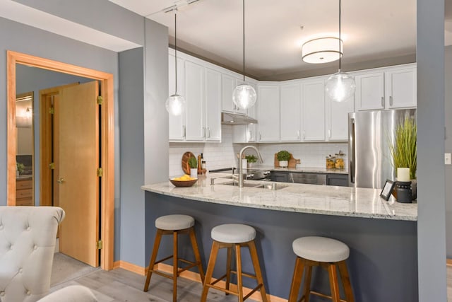 kitchen featuring stainless steel fridge, a sink, light stone countertops, and decorative backsplash