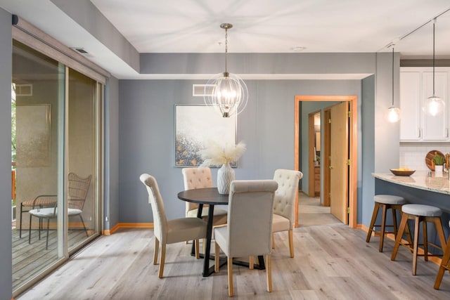 dining room featuring a chandelier, light wood finished floors, rail lighting, and baseboards
