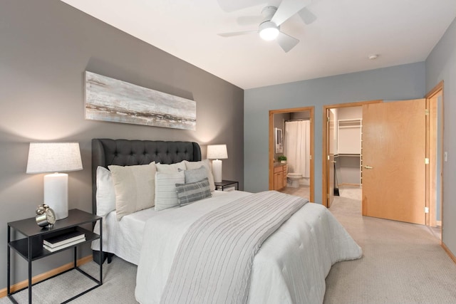 bedroom with light carpet, a walk in closet, ensuite bathroom, baseboards, and a ceiling fan