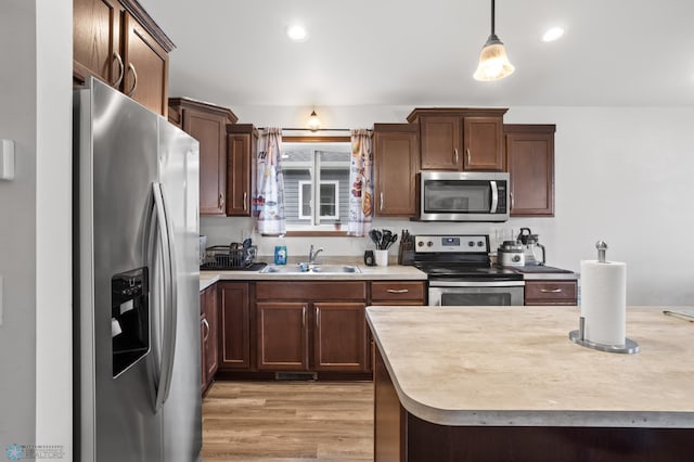kitchen featuring appliances with stainless steel finishes, a sink, light countertops, light wood finished floors, and recessed lighting