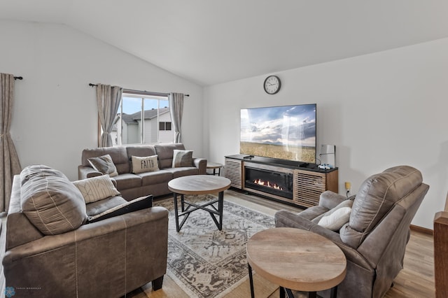 living area featuring vaulted ceiling, light wood finished floors, and a glass covered fireplace