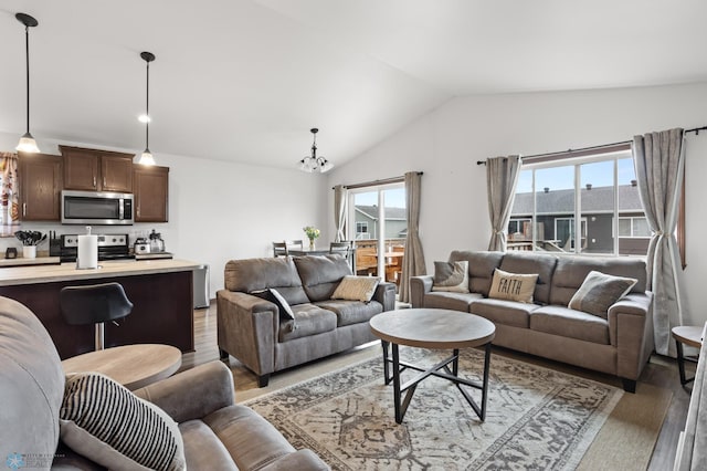 living room featuring light wood-style flooring, vaulted ceiling, healthy amount of natural light, and a chandelier