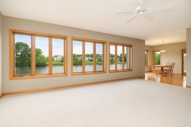 carpeted spare room with a water view, baseboards, ceiling fan, and wood finished floors