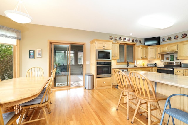 kitchen with appliances with stainless steel finishes, light brown cabinets, light wood-type flooring, a kitchen breakfast bar, and under cabinet range hood