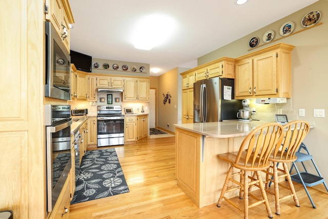 kitchen with stainless steel appliances, light brown cabinetry, a peninsula, light countertops, and light wood-type flooring