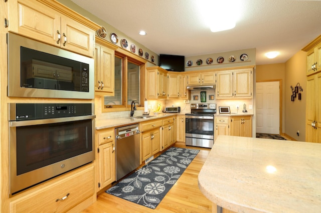 kitchen with stainless steel appliances, a sink, under cabinet range hood, light wood-style flooring, and recessed lighting