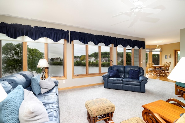 living room featuring ceiling fan, carpet, baseboards, and a water view